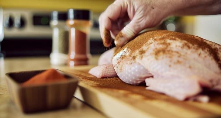 Applying dry rub seasoning to turkey before smoking