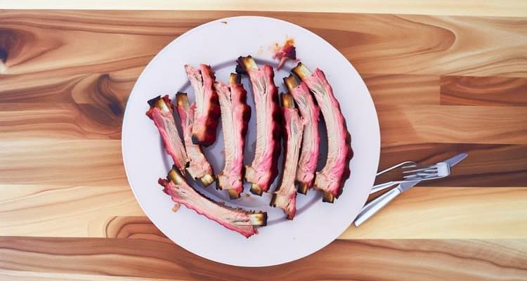 Sliced smoked pork ribs on white plate showing pink smoke ring and tender meat pulling from bones