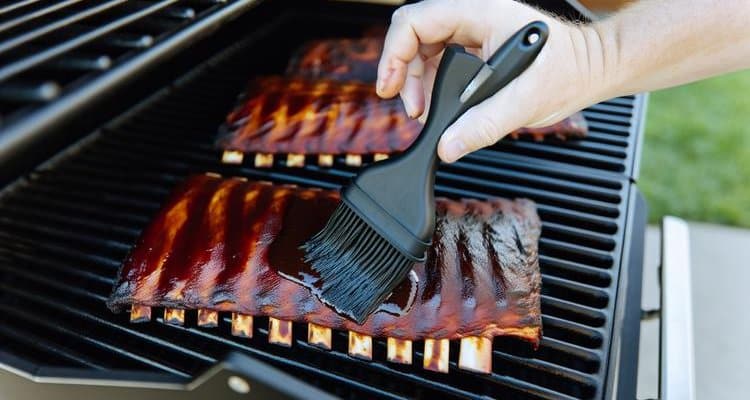 Hand brushing BBQ sauce onto smoked ribs with basting brush during Phase 3 final glazing step