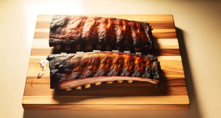 Perfectly smoked pork ribs with dark mahogany bark and visible smoke ring on wooden cutting board