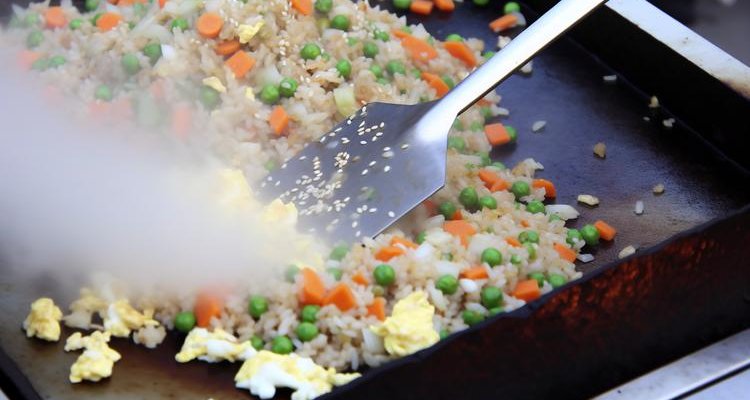 Fried rice with colorful vegetables being stirred on Blackstone griddle with metal spatula and sesame seeds