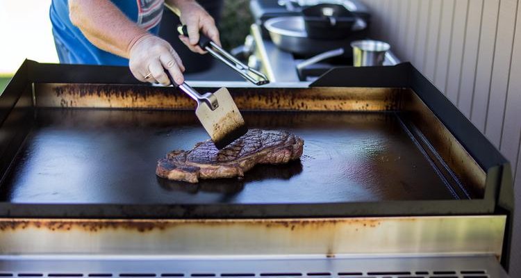 Flipping ribeye steak on Blackstone griddle showing perfect dark brown crust formation