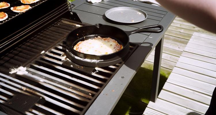 Pizza on cast iron pan on outdoor grill with cheese bubbling cooking process