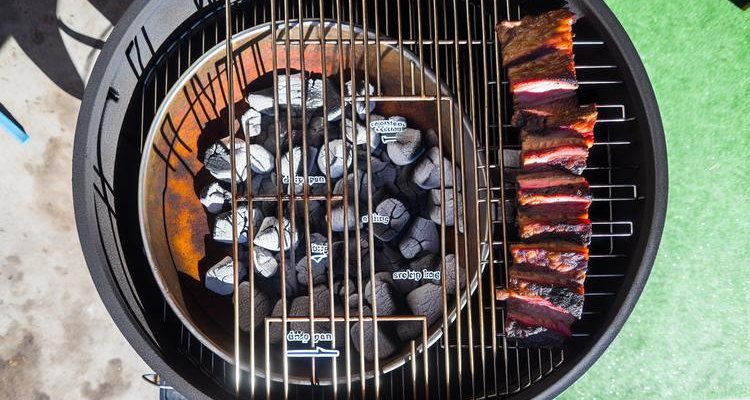 Overhead view showing proper drip pan placement for indirect cooking on charcoal grill with ribs