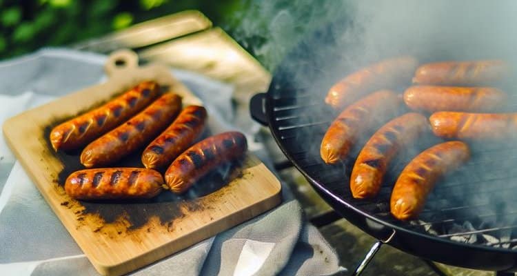 Finished golden-brown smoked sausages resting on cutting board with smoke wisps, ready to serve