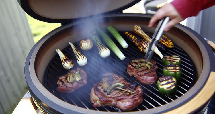 Steaks and vegetables grilling on kamado with visible smoke showcasing versatile cooking capability