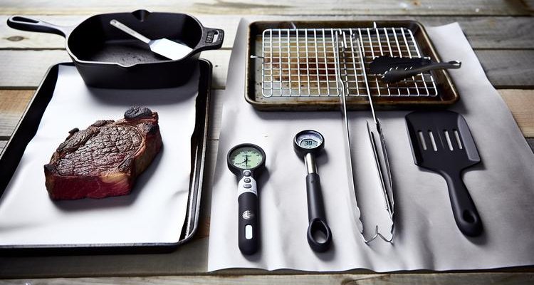 Essential equipment for reverse searing including cast iron skillet, wire rack, meat thermometer, and thick steak