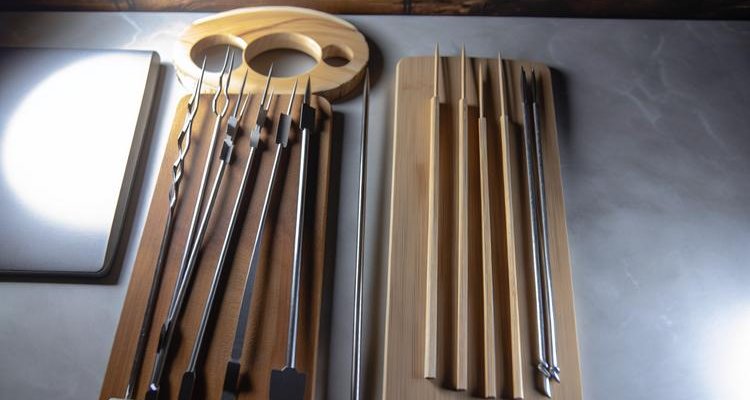 Educational flat lay of different skewer types - flat metal, round metal, bamboo, and double prong skewers displayed on wooden cutting board