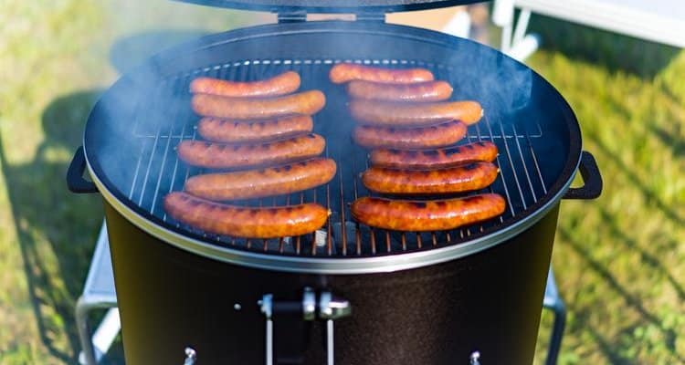 Perfectly smoked sausages on smoker grill with visible smoke and golden-brown color