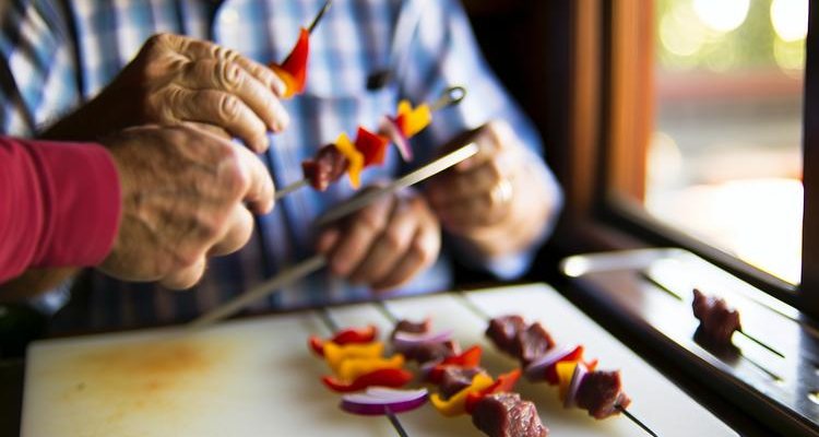 Close-up of hands demonstrating proper threading technique with beef and colorful vegetables on metal skewer showing even spacing