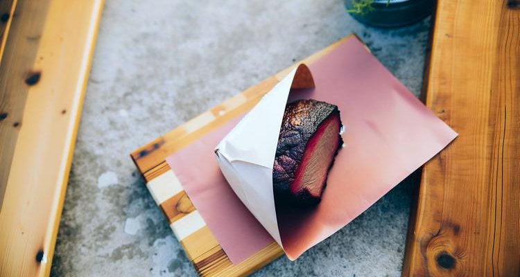 perfectly smoked brisket wrapped in pink butcher paper on cutting board with beautiful mahogany crust visible
