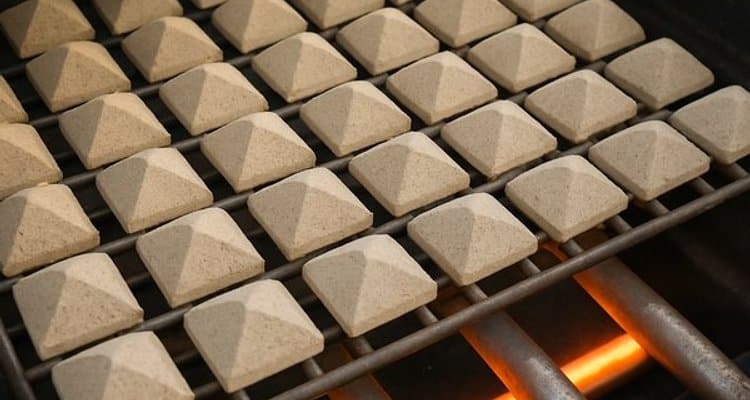 Close-up of uniform tan ceramic briquettes arranged on rock grate inside gas grill above burners