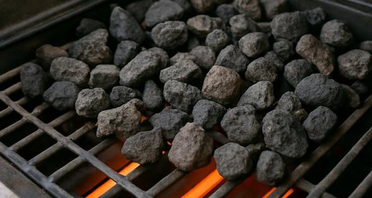 Close-up of dark porous lava rocks installed on rock grate inside gas grill above burners