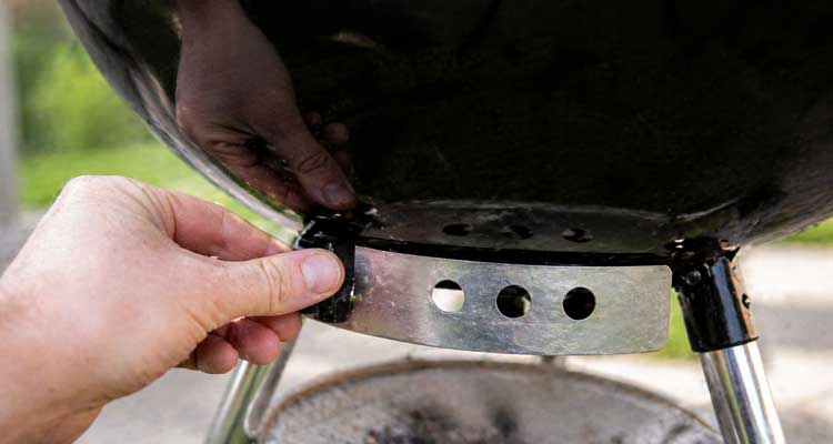 Hand adjusting charcoal grill temperature