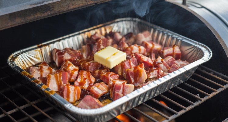 Cubed bacon pieces in aluminum pan with BBQ sauce glaze and melting butter on a smoker