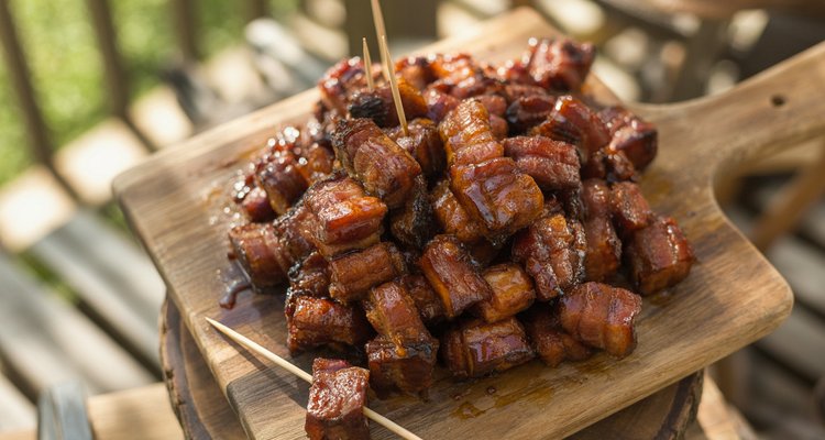 Glossy caramelized bacon burnt ends piled on a rustic wooden cutting board with toothpicks