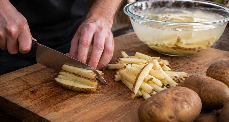 Cast iron Dutch oven filled with beef tallow with spider strainer lifting pale blanched fries