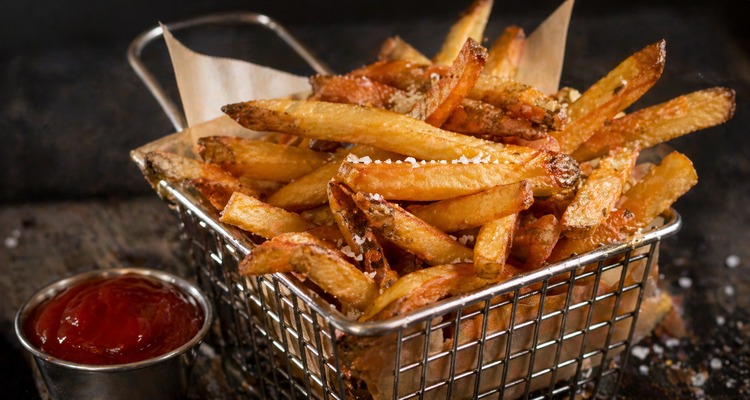 Golden crispy beef tallow french fries in a wire basket with coarse sea salt and ketchup
