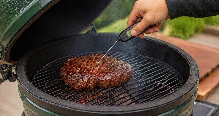 Pitmaster using an instant-read thermometer to check the temperature of a thick steak on a kamado grill