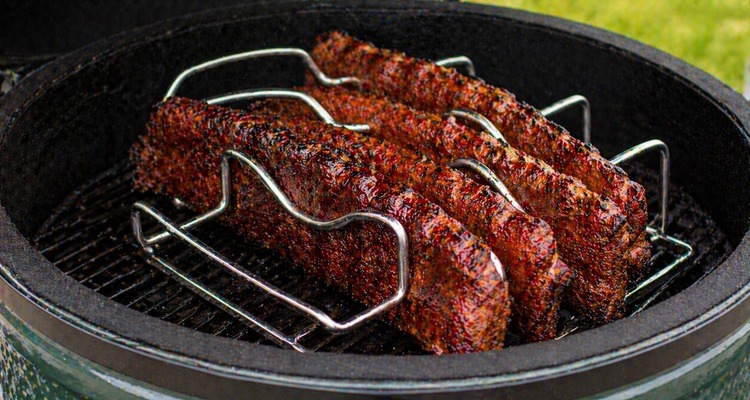 Stainless steel rib rack holding multiple racks of ribs inside a ceramic kamado grill
