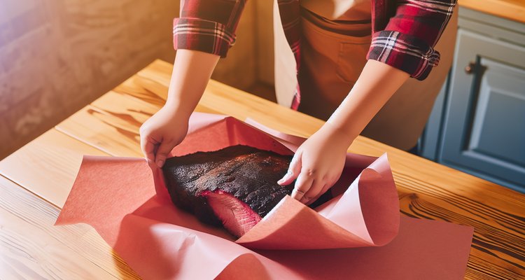 Wrapping brisket in pink butcher paper on a wooden table showing the dark bark before wrapping