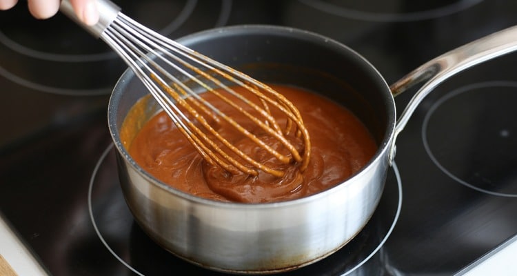 Buffalo sauce being whisked in a saucepan over low heat until smooth and glossy