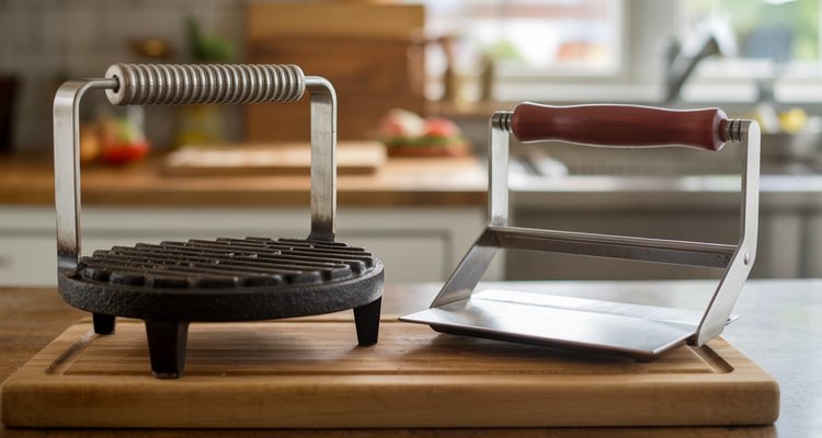 Cast iron burger press and stainless steel burger press side by side on a wooden cutting board