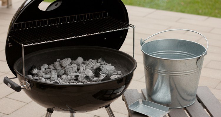 Cold ash in a charcoal grill with a metal ash bucket ready for disposal
