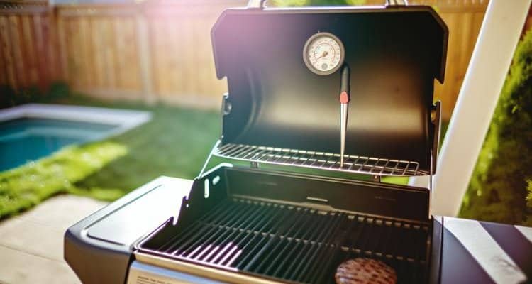 Gas grill with thermometer checking burger temperature in backyard setting