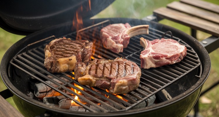 Steaks and chops searing on cast iron grill grates over charcoal flames on a heavy duty charcoal grill