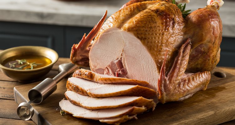 Brined and injected whole roasted turkey with carved slices showing juicy meat on a wooden cutting board
