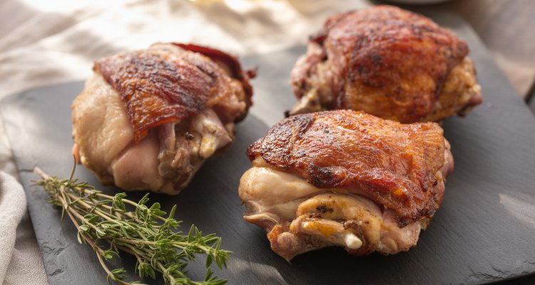Smoked chicken thighs on slate board Three bone-in smoked chicken thighs on a dark slate board with crispy golden skin and fresh thyme sprigs