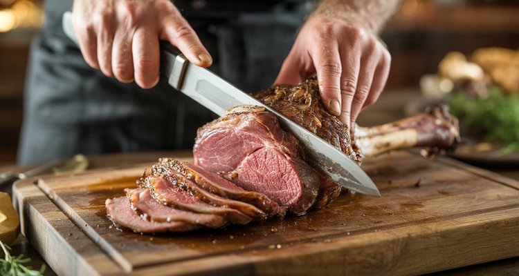 Hands carving a smoked leg of lamb revealing juicy pink interior on a wooden cutting board