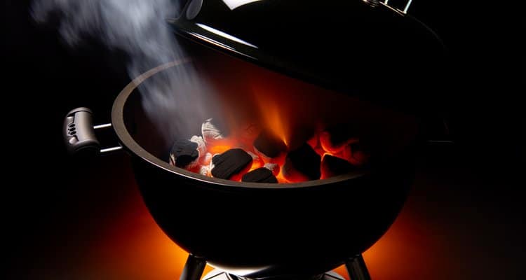 Medium charcoal kettle grill with glowing coals and smoke rising in moody BBQ atmosphere
