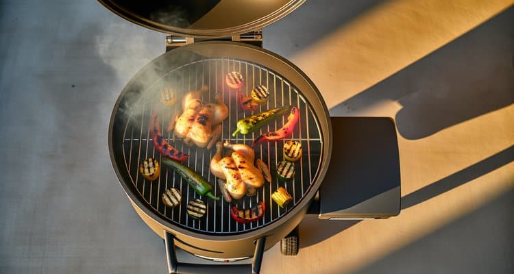 Overhead view of a medium pellet grill loaded with chicken and vegetables in golden hour light