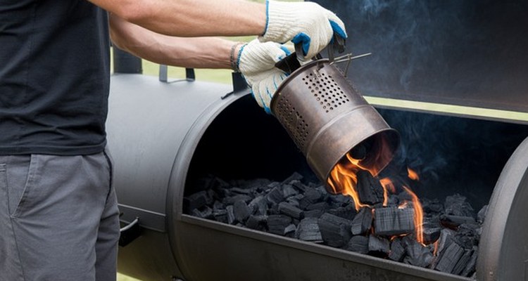 Gloved hands pouring lit charcoal into an offset smoker firebox