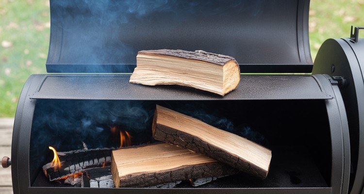 Single hardwood split prewarming on an offset smoker firebox with a fire below