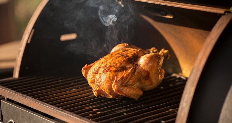 Whole smoked chicken on pellet grill grates with golden-brown bark and white smoke wisps rising