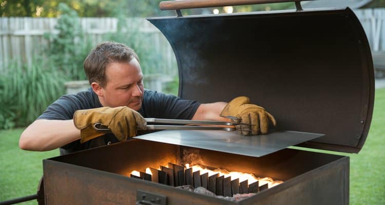 Person adjusting steel baffle plates inside offset smoker cook chamber