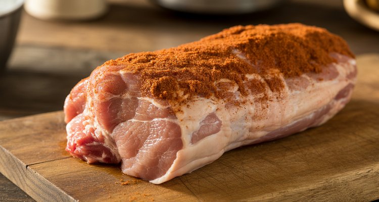 Applying dry rub to pork tenderloin Brown sugar and paprika dry rub being applied to a raw pork tenderloin on a cutting board
