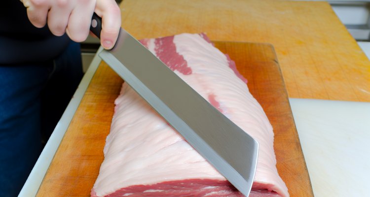 Boning knife trimming the fat cap of a raw brisket to quarter-inch thickness with a long sweeping stroke