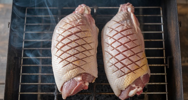Two scored duck breasts with crosshatch pattern on smoker grate with wisps of smoke