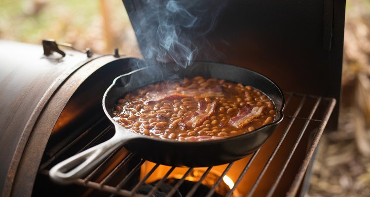 Baked beans smoking on the grill grates Cast iron skillet of baked beans sitting on smoker grates with smoke rising around it