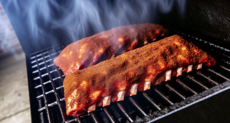 Beef back ribs coated in dry rub seasoning on smoker grates with white smoke