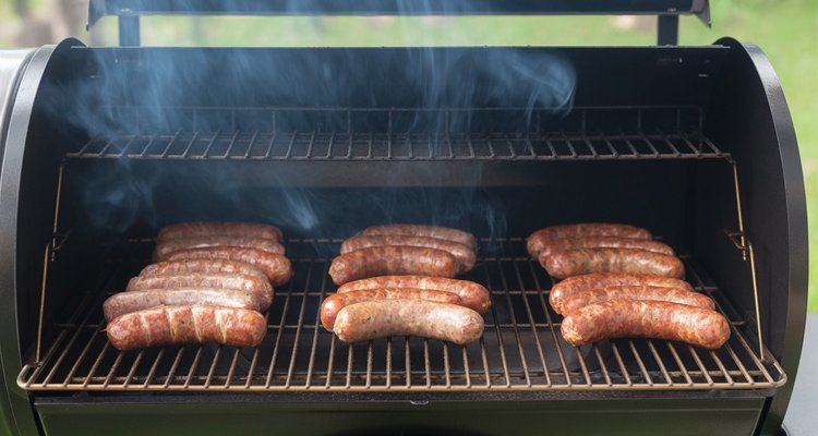 Uncooked brats spaced on pellet grill grates with thin blue smoke rising