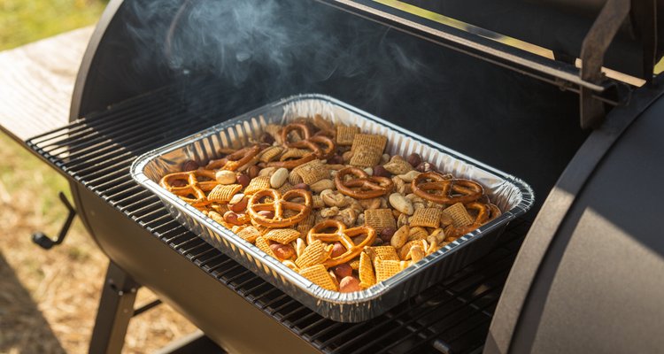 Smoked Chex Mix in an aluminum pan on a pellet smoker with wisps of smoke