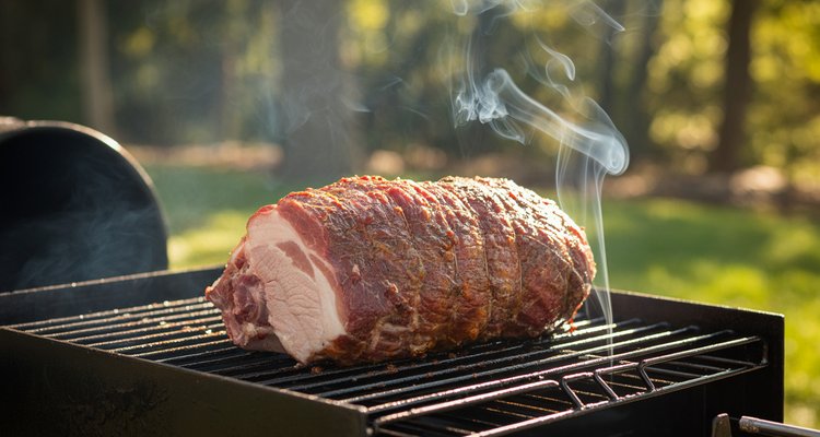 Whole pork loin on smoker grates with visible smoke rising