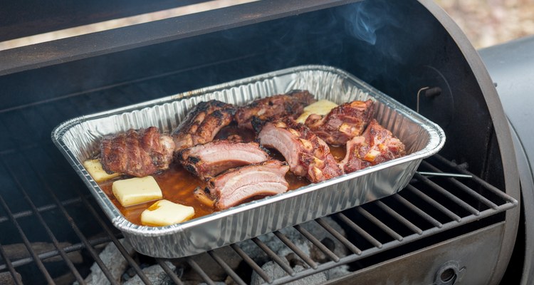 Smoked pork rib tips braising with apple juice and butter in a foil pan on smoker grates