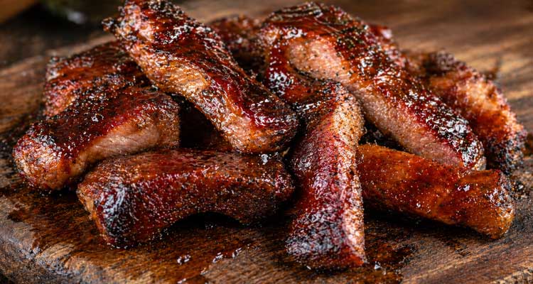 Smoked Rib Tips glazed in sticky BBQ sauce on a rustic wooden cutting board