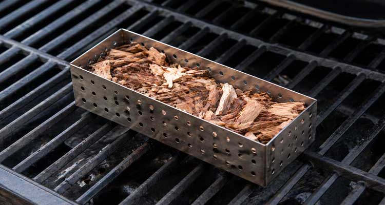 Smoker box filled with wood chips on a gas grill